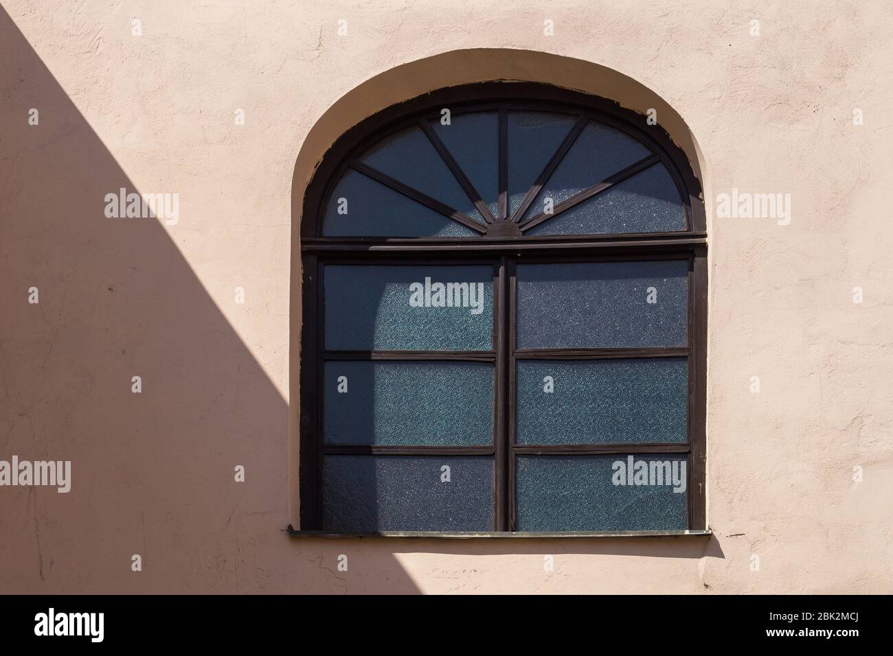 Wooden brown frame of a window with an arc. Light orange wall, enlightened by the sunlight with a diagonal shadow, touching a corner of the window. Br Stock Photo