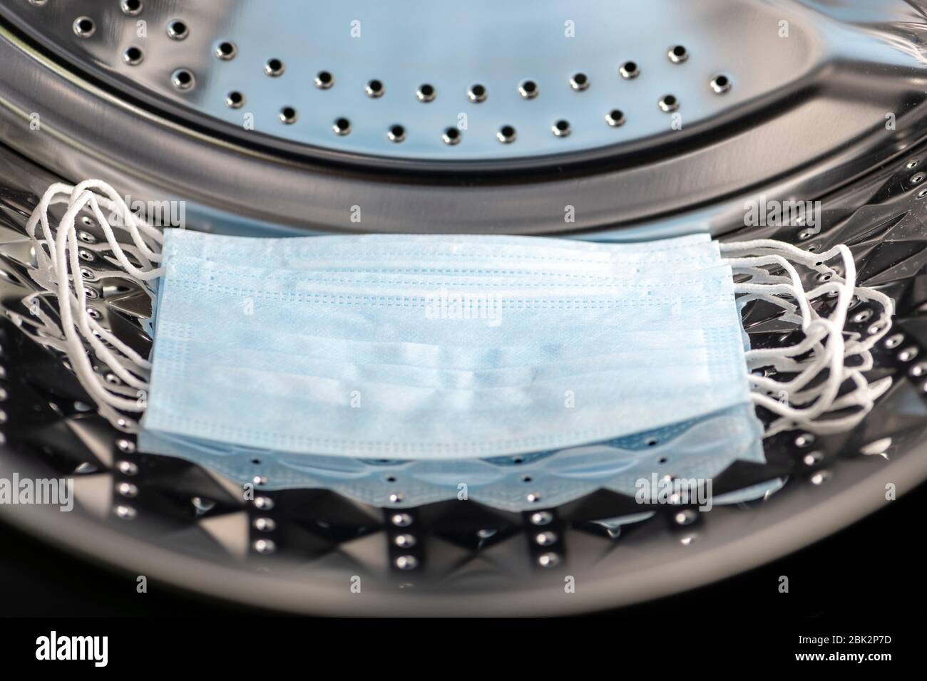 PPE face masks in a washing machine. Concept of PPE shortages & re-use. Wash face mask due to PPE supply problems, UK. Stock Photo