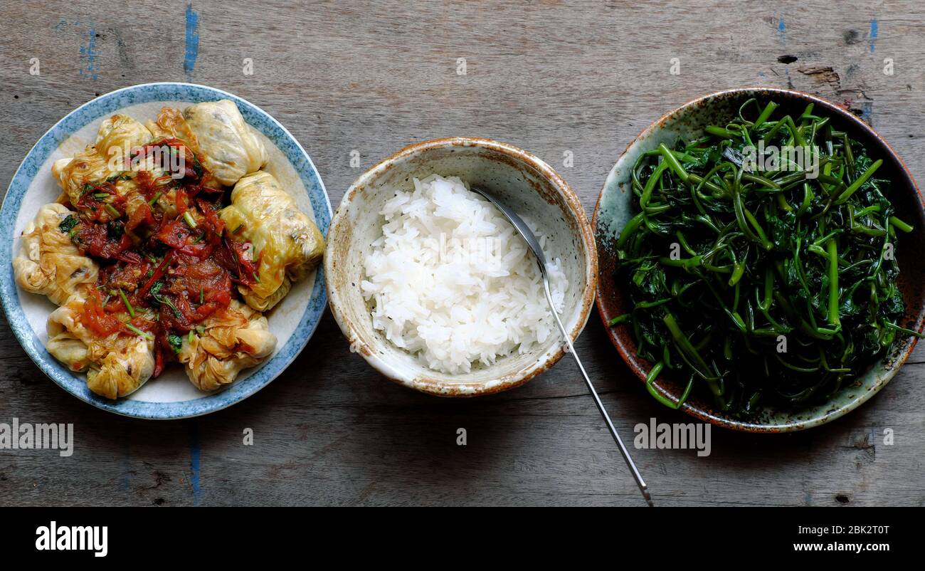 Simple Vietnamese vegan meal for lunch, boiled water spinach, stuffed cabbage with tomato sauce, bowl of rice, healthy food that rich fiber Stock Photo
