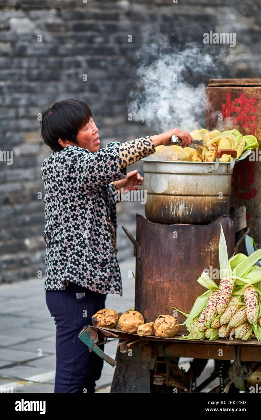 Qufu / China - October 13, 2018: Woman cooking corn clips on a street food stall in Qufu, birthplace of philosopher Confucius, Shandong province, Chin Stock Photo