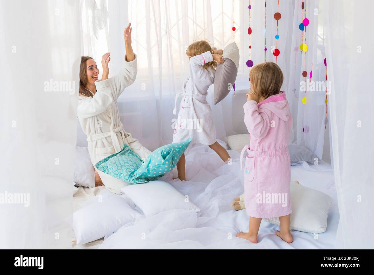 Young woman have fun with the children playing with pillows on the bed