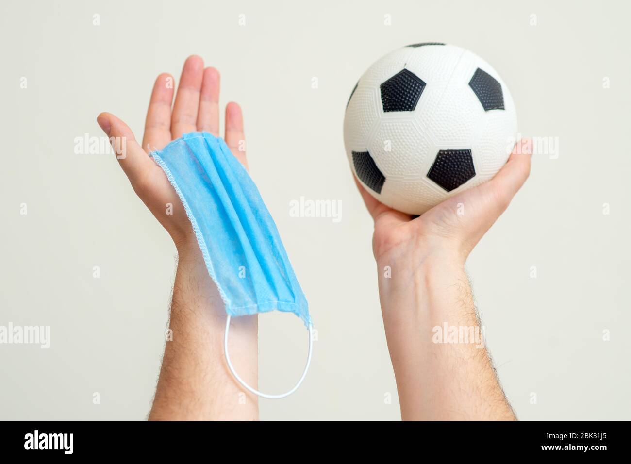 Soccer ball and medical mask in man hands up on white background. Stock Photo