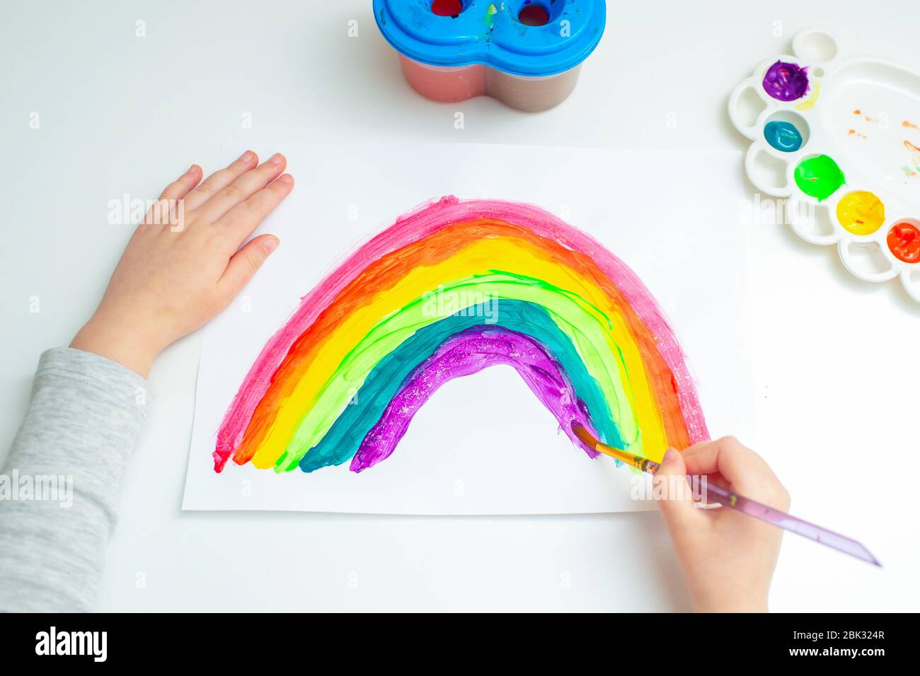 Top view child is drawing rainbow with watercolors on the sheet of paper. Creativity concept. Stock Photo