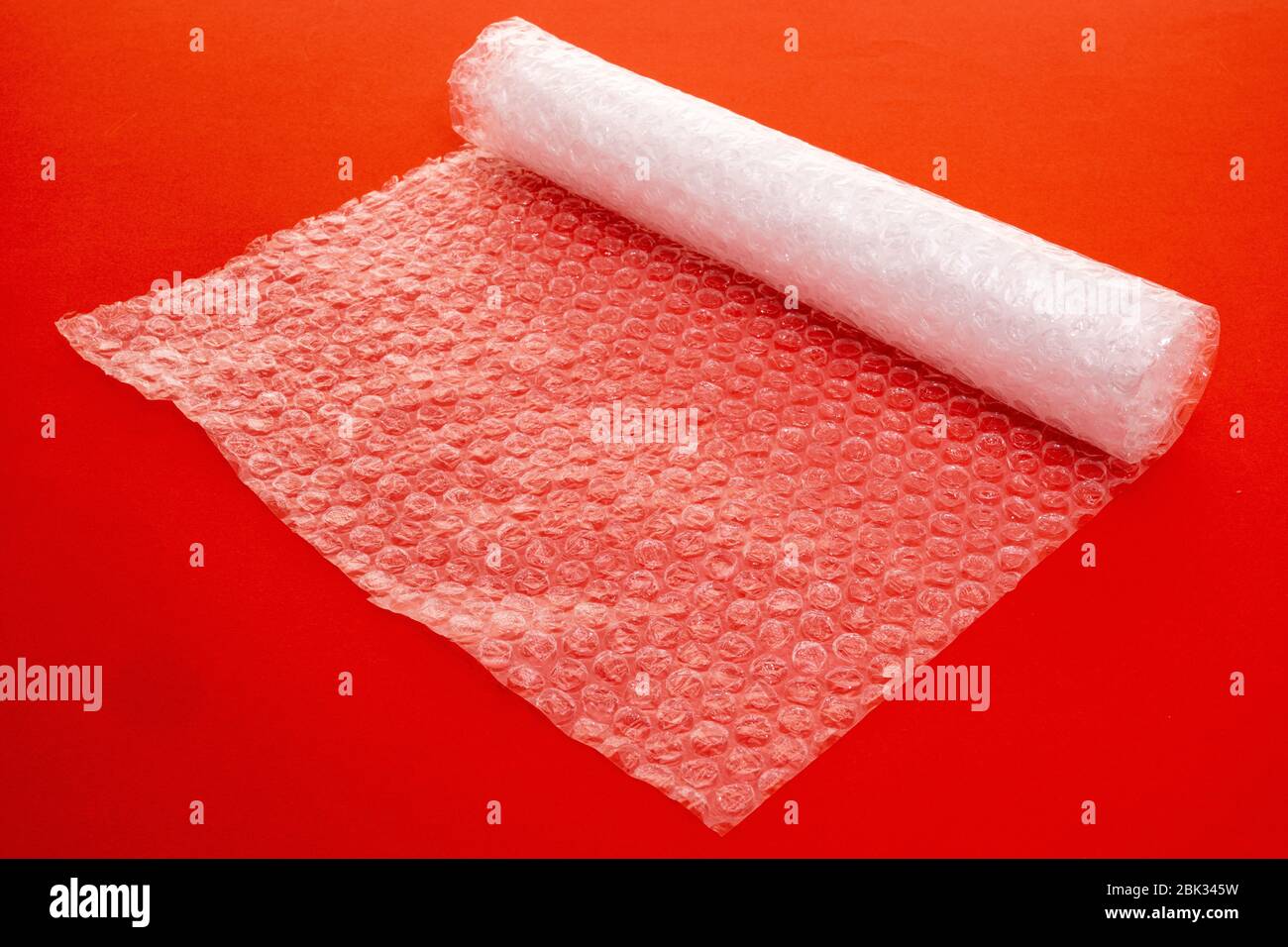 Clear plastic bubble wrap packaging stretched out over a plain red background - studio shot Stock Photo