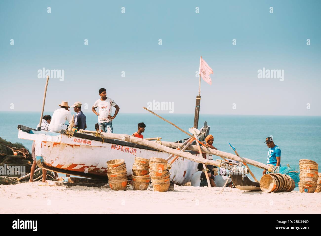 Arossim, Goa, India - February 18, 2020: Fishermen Resting Near Pulled Boat From Sea Stock Photo