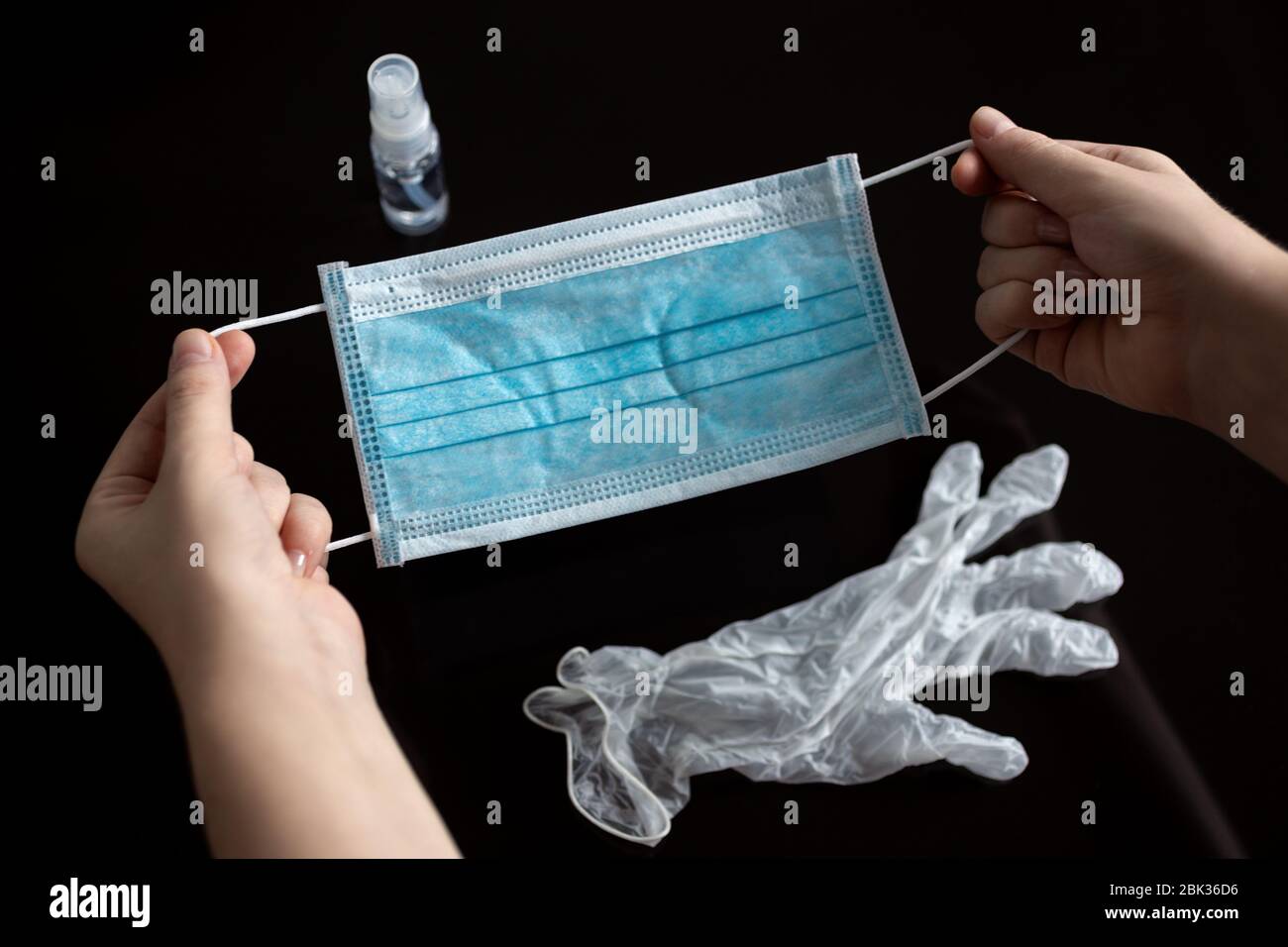 Hands holding surgical face mask, gloves and alcohol during the coronavirus covid-19 quarantine. Black background Stock Photo