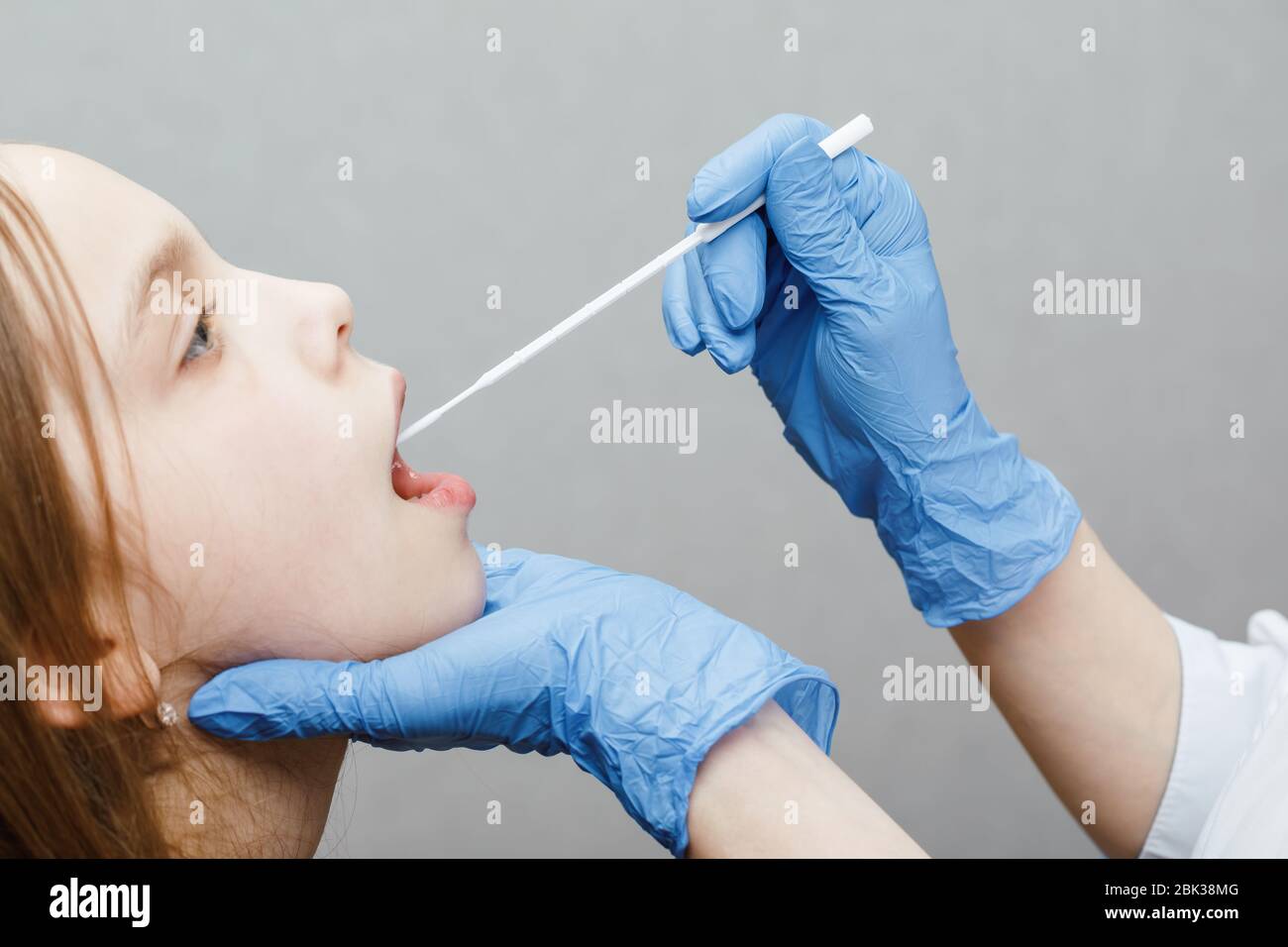 Pediatrician taking saliva test sample from elementary age girl's mouth performing Saliva testing (Salivaomics) diagnostic procedure Stock Photo