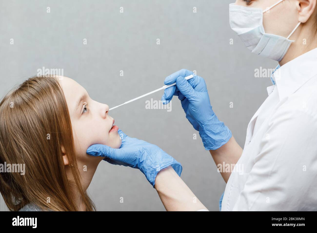 Pediatrician taking nasal mucus test sample from elementary age girl's nose performing respiratory virus testing procedure Stock Photo