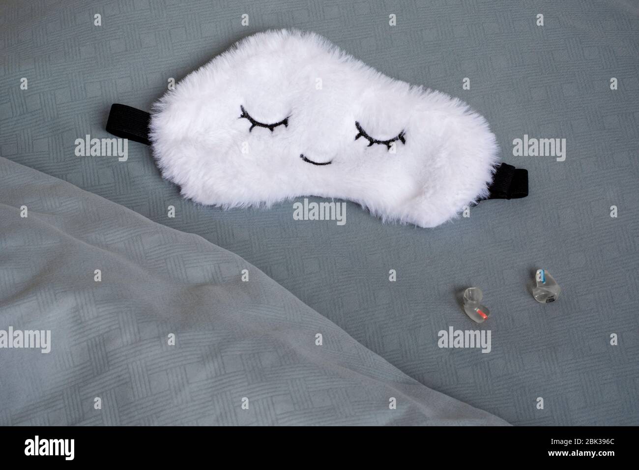 White cute sleep mask made of fluffy faux fur in a cloud shape with closed eyes embroidered on it and custom molded sleep ear plugs Stock Photo
