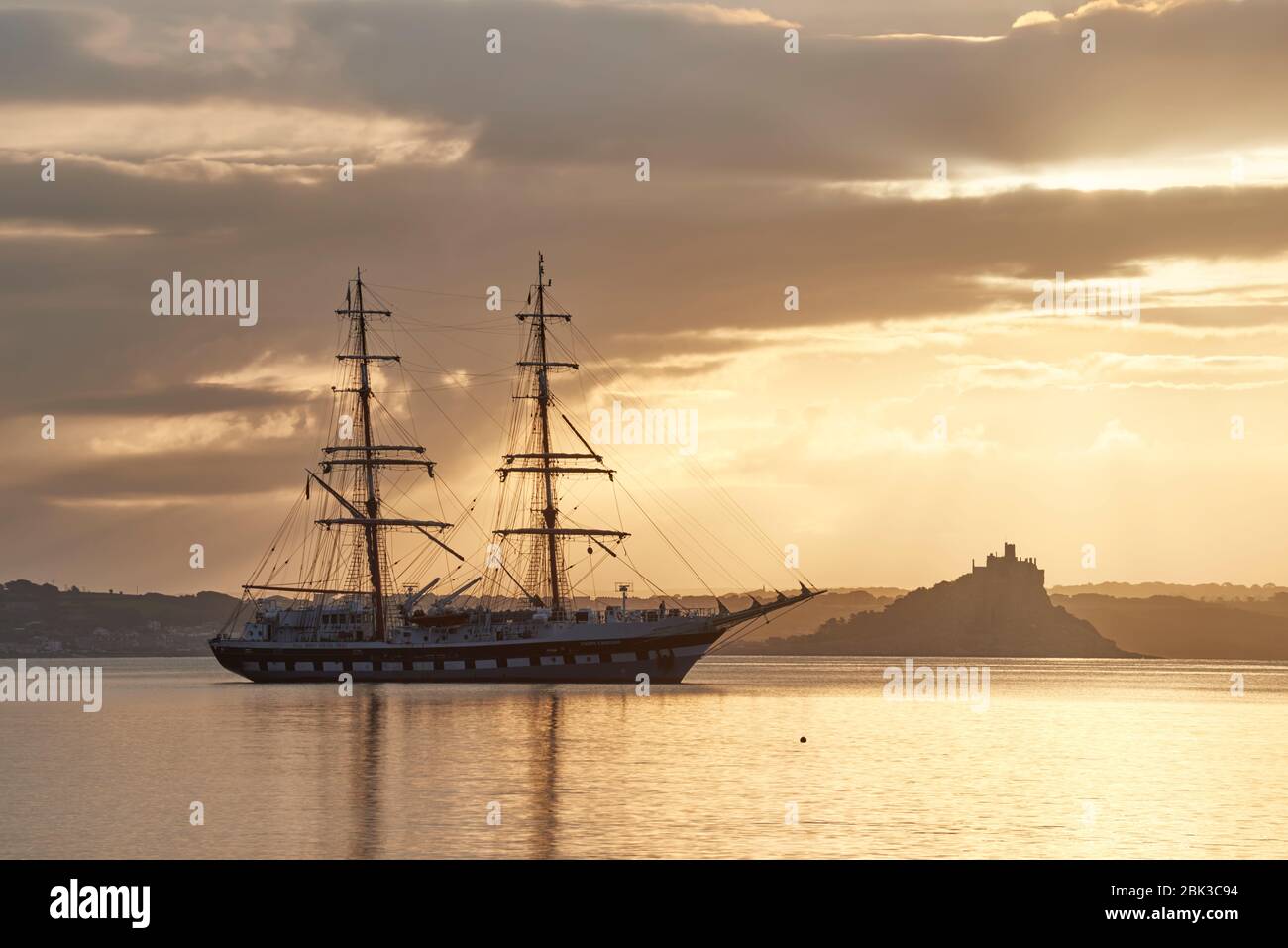 Tall Ship anchored in Mounts Bay Cornwall on calm still morning with St Michael's Mount Silhouetted across the bay Stock Photo