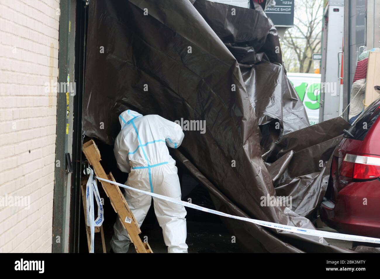 New York, New York, USA. 30th Apr, 2020. A worker dressed in a hazmat rushes under the brown tarp set up from the back of a truck to the entrance of the Andrew T. Cleckley Funeral Home in Brooklyn where bodies non properly cared are removed. 60 corpses were stored in 4 non-refregerated rented vehiciles lining the street along stores. Neighbors reported a foul smell and fluids dripping from the trucks. The funeral home was overwhelmed by COVID-19 deaths and ran out of room for bodies, which were awaiting cremation in New York. Credit: Marie Le Ble/ZUMA Wire/Alamy Live News Stock Photo