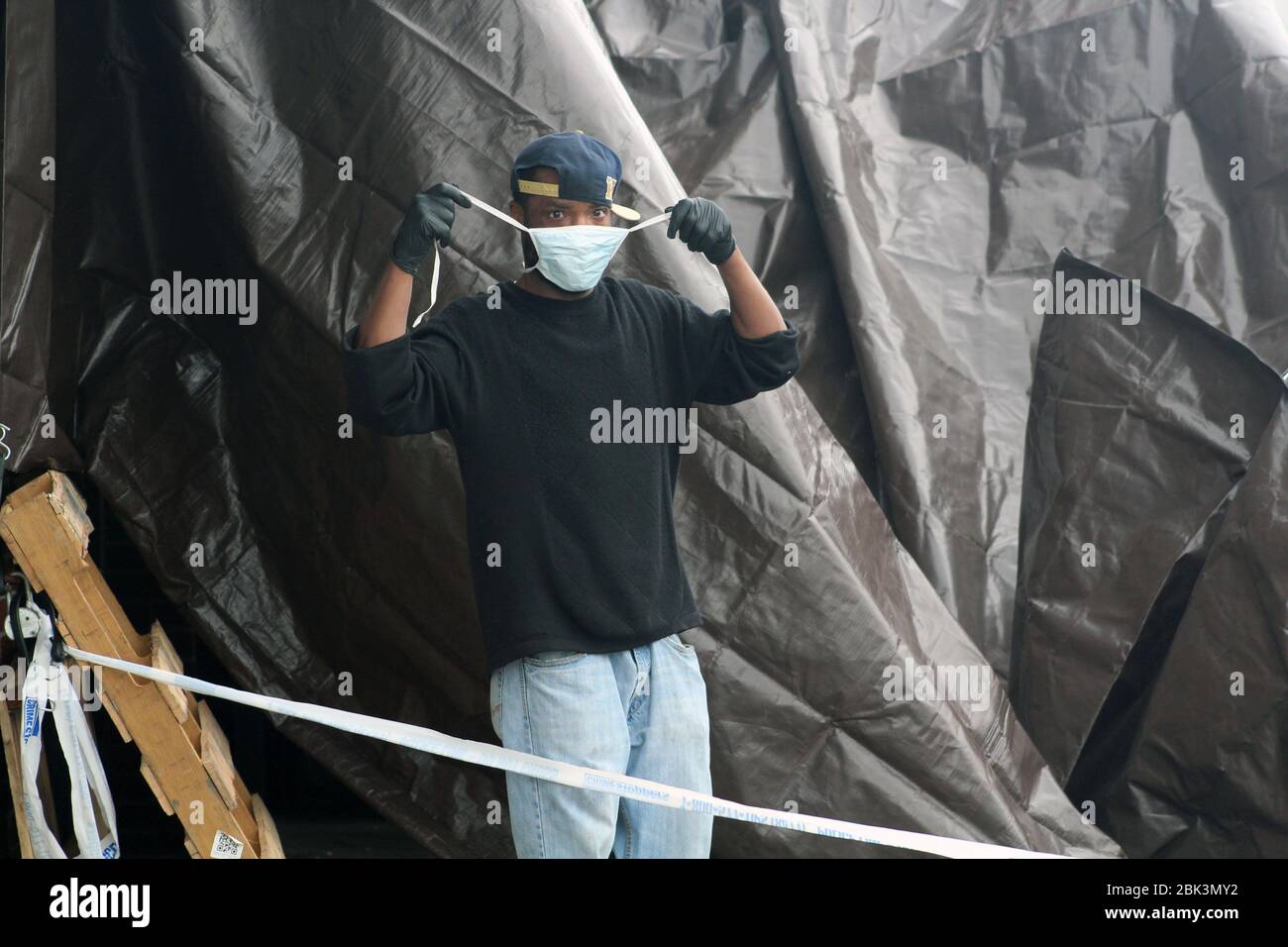 April 30, 2020, New York, New York, USA: Gloved hands, a worker adjusts his protective mask along a brown tarp set up at the entrance of the Andrew T. Cleckley Funeral Home in Brooklyn where bodies non properly cared are removed. 60 corpses were stored in 4 non-refregerated vehiciles lining the street nearby stores. Neighbors reported a foul smell still persistent and fluids dripping from the trucks. The funeral home was overwhelmed by COVID-19 deaths, waiting for weeks for cremations in New York. (Credit Image: © Marie Le Ble/ZUMA Wire) Stock Photo