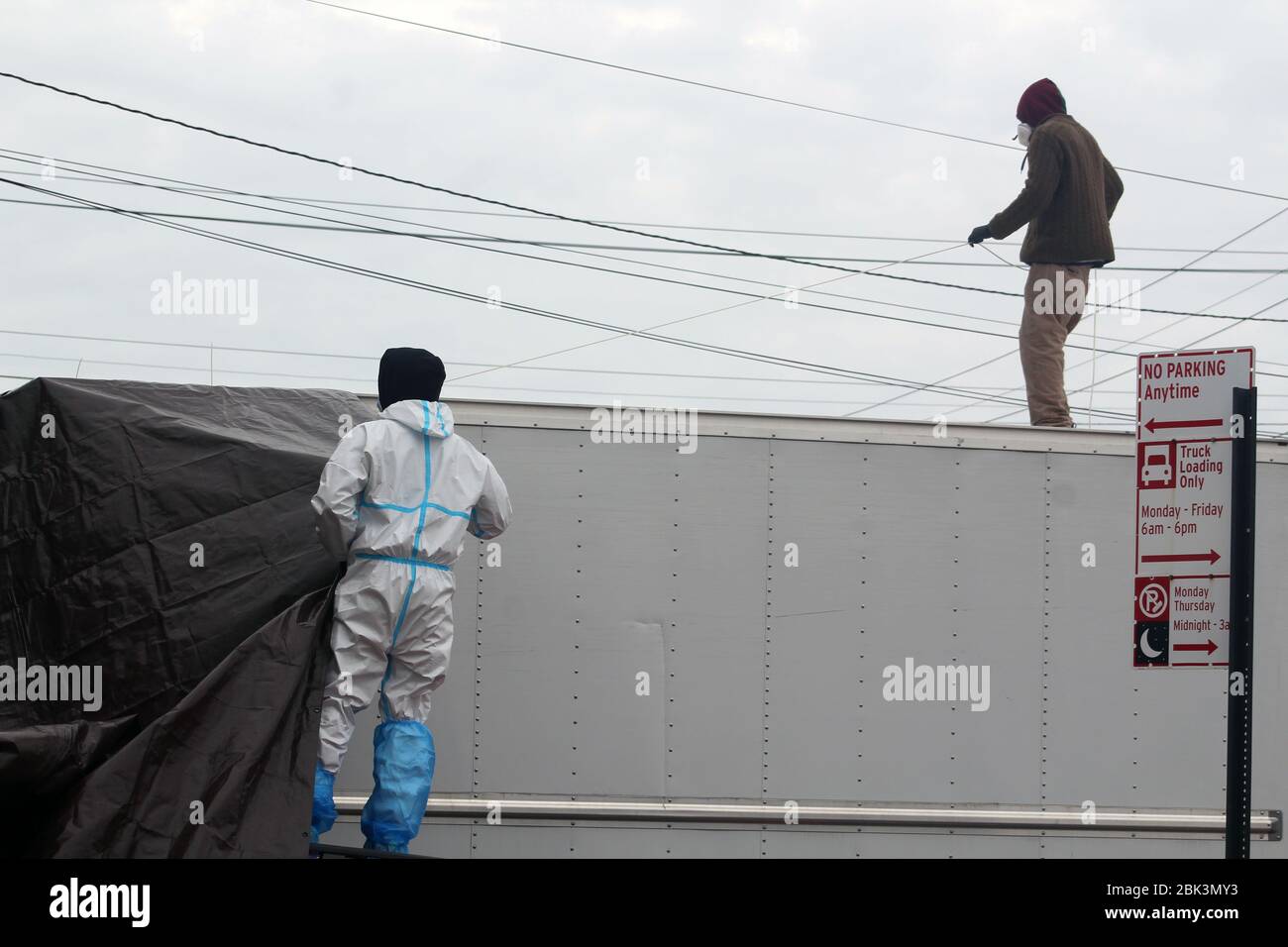 April 30, 2020, New York, New York, USA: One of these 2 workers climbed on the roof of a large refrigerated truck to deploy a tarp in front of the Andrew T. Cleckley Funeral Home in Brooklyn where bodies not properly cared are removed. 60 corpses were stored in 4 non-refrigerated trucks lining the street along stores. Neighbors reported a foul smell and fluids dripping from the trucks. Some remains were also found lying on the facilityÃ¢â‚¬â„¢s floor. In New York City alone, there have been almost 13,000 COVID-19 deaths. (Credit Image: © Marie Le Ble/ZUMA Wire) Stock Photo