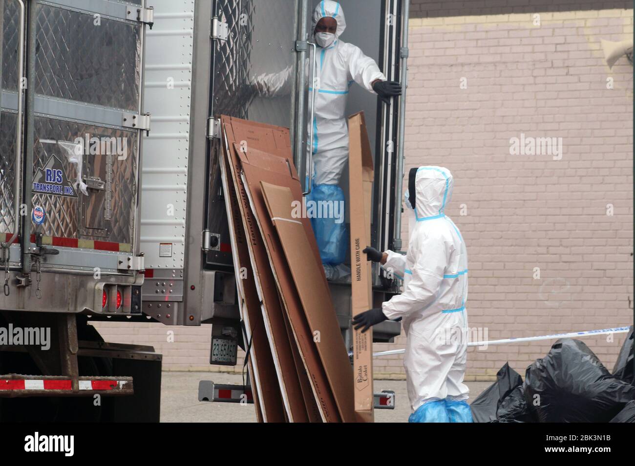 April 30, 2020, New York, New York, USA: These 2 men dressed in a hazmat, take cardboard coffins from a large refrigerated truck where bodies are stored next to the Andrew T. Cleckley Funeral Home in Brooklyn whose corpses not properly cared have been removed. 60 bodies were stored in 4 non-refregerated vehiciles lining the street nearby stores. Neighbors reported a foul smell still persistent and fluids dripping from the trucks. The funeral home was overwhelmed by COVID-19 deaths, waiting for weeks for cremations in New York. (Credit Image: © Marie Le Ble/ZUMA Wire) Stock Photo