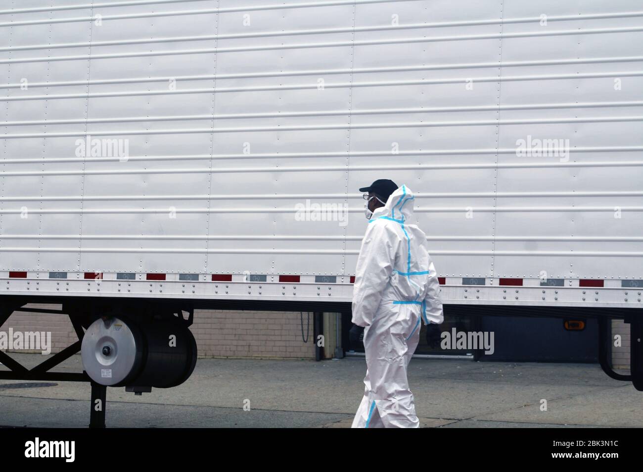 April 30, 2020, New York, New York, USA: This worker, dressed in a hazmat, runs alongside a large refrigerated truck parked in front of the Andrew T. Cleckley Funeral Home in Brooklyn where bodies non properly cared are removed. 60 corpses were stored in 4 rented vehiciles lining the street nearby stores. Neighbors reported a foul smell still persistent and fluids dripping from the trucks. Some remains were also found lying on the facilityÃ¢â‚¬â„¢s floor. The funeral home was overwhelmed by COVID-19 deaths, waiting for weeks for cremations in New York. (Credit Image: © Marie Le Ble/ZUMA Wire) Stock Photo