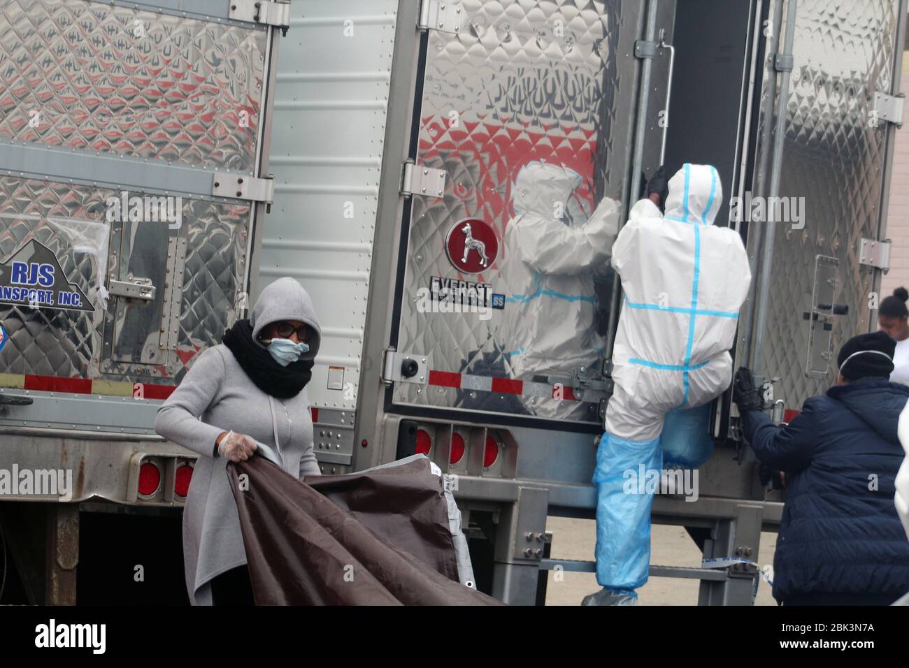 New York, New York, USA. 30th Apr, 2020. This man, dressed in a hazmat, climbs in one of the big refrigerated trucks where bodies have been disposed next to the Andrew T. Cleckley Funeral Home in Brooklyn whose corpses not properly cared have been removed. Meanwhile an employee, masked face, deploys a brown tarpaulin. 60 bodies were stored in 4 non-refregerated vehiciles lining the street nearby stores. Neighbors reported a foul smell still persistent and fluids dripping from the trucks. The funeral home was overwhelmed by COVID-19 deaths, waiting for weeks for cremations in New York. (Credit Stock Photo