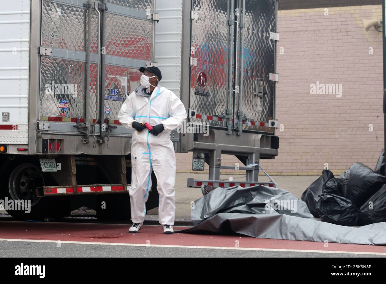 New York, New York, USA. 30th Apr, 2020. This man, dressed in a hazmat and masked face, stands in front of the doors of 2 big refrigerated trucks drove to the Andrew T. Cleckley Funeral Home in Brooklyn where corpses not properly cared have been removed. 60 bodies were stored in 4 non-refregerated vehiciles lining the street nearby stores. Neighbors reported a foul smell still persistent and fluids dripping from the trucks. The funeral home was overwhelmed by COVID-19 deaths, waiting for weeks for cremations in New York. Credit: Marie Le Ble/ZUMA Wire/Alamy Live News Stock Photo