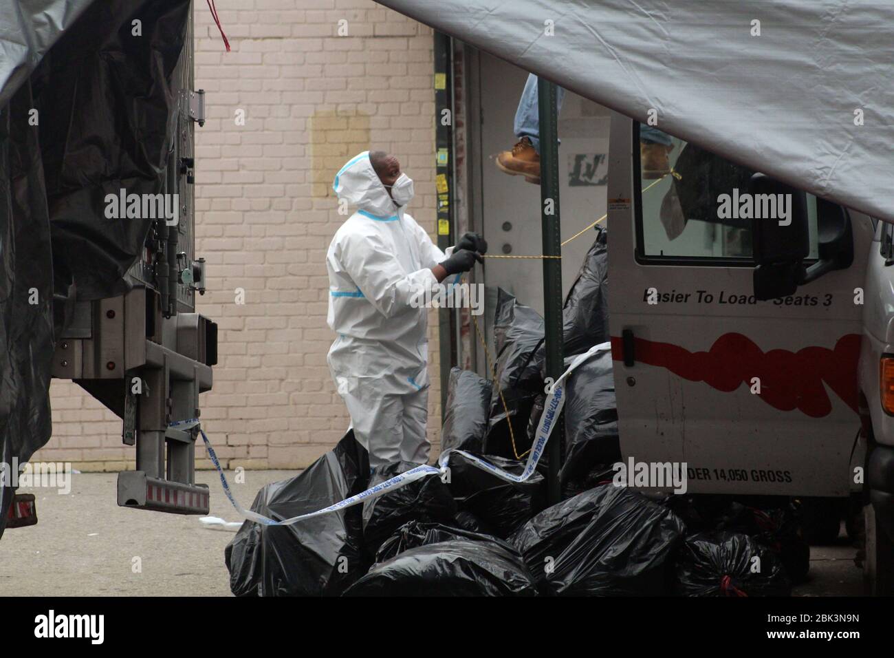 April 30, 2020, New York, New York, USA: This man, dressed in a hazmat, pulls a cord in the middle of large black trash bags to set up a tarpaulin at the back of a refrigerated truck next to the Andrew T. Cleckley Funeral Home in Brooklyn where corpses not properly cared have been removed. 60 bodies were stored in 4 non-refregerated vehiciles lining the street nearby stores. Neighbors reported a foul smell still persistent and fluids dripping from the trucks. The funeral home was overwhelmed by COVID-19 deaths, waiting for weeks for cremations in New York. (Credit Image: © Marie Le Ble/ZUMA Wi Stock Photo