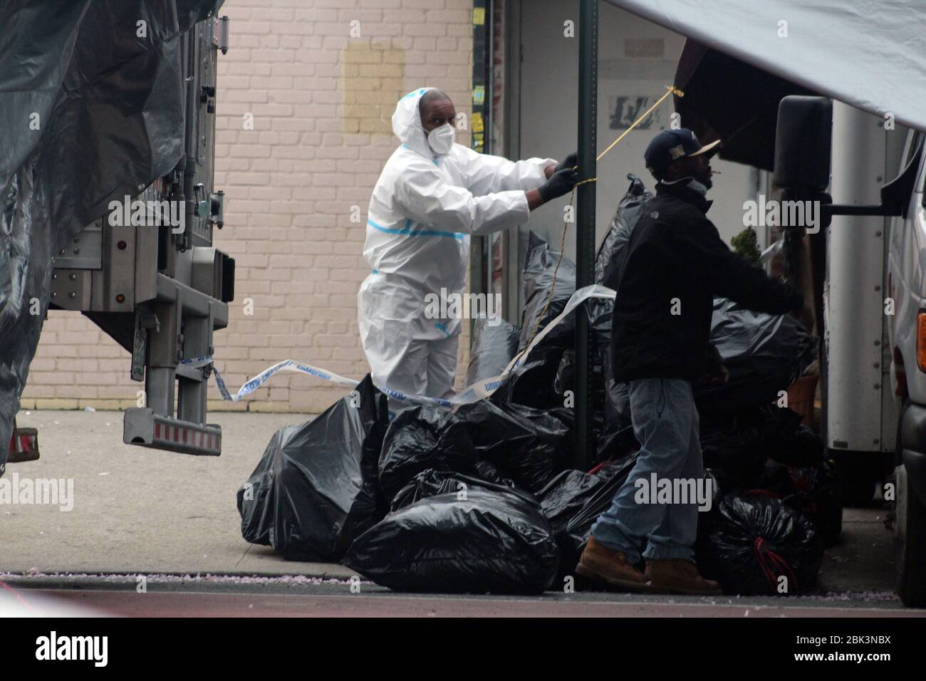 April 30, 2020, New York, New York, USA: This man, dressed in a hazmat, pulls a cord in the middle of large black trash bags to install tarpaulin at the back of a refrigerated truck next to the Andrew T. Cleckley Funeral Home in Brooklyn where corpses not properly cared have been removed. 60 bodies were stored in 4 non-refregerated vehiciles lining the street nearby stores. Neighbors reported a foul smell still persistent and fluids dripping from the trucks. The funeral home was overwhelmed by COVID-19 deaths, waiting for weeks for cremations in New York. (Credit Image: © Marie Le Ble/ZUMA Wir Stock Photo