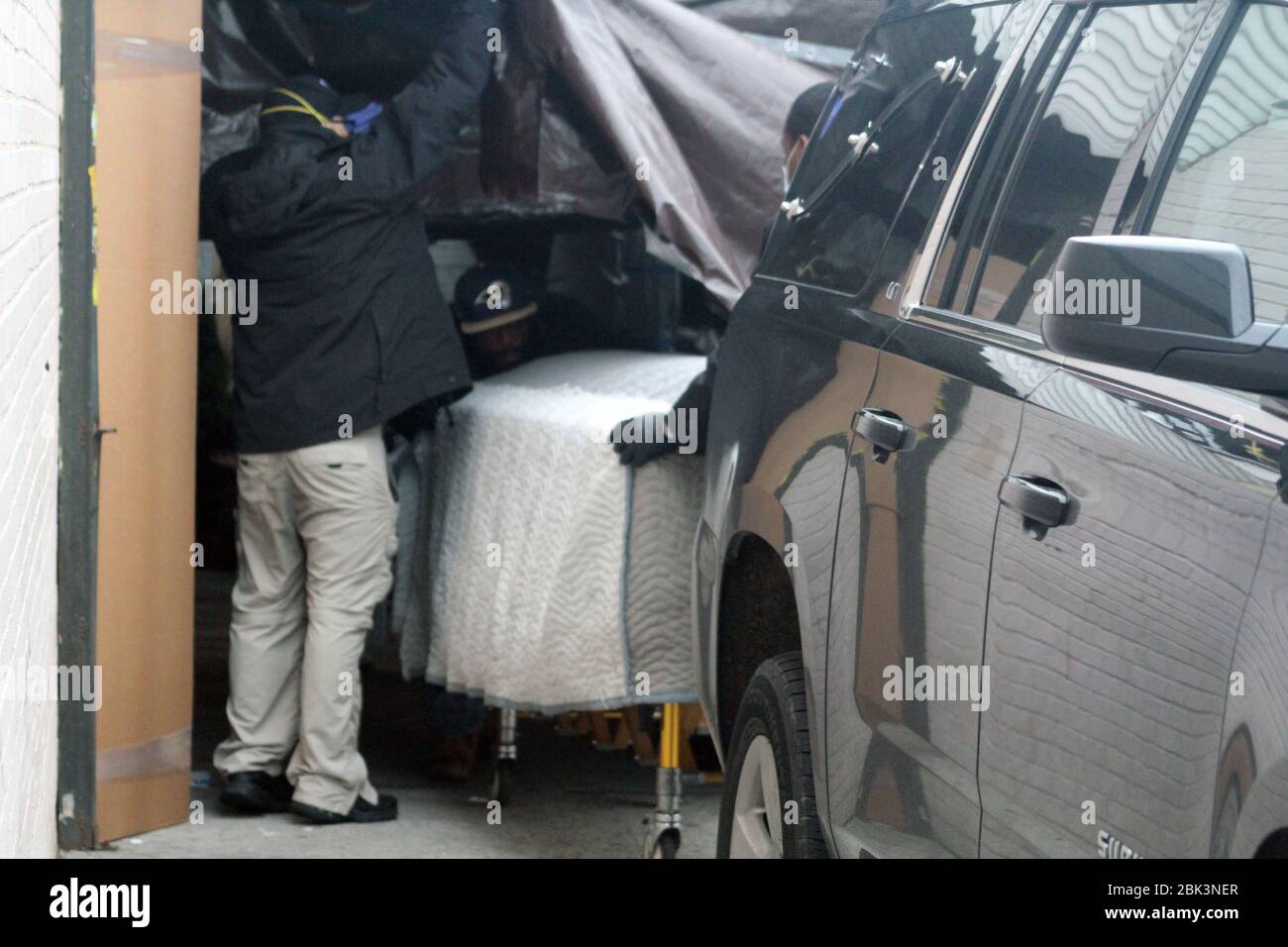 April 30, 2020, New York, New York, USA: An employee in the back pushes on a coffin covered with a white cloth, helped by a mortician while a man lifts a brown tarp set up in front of the Andrew T. Cleckley Funeral Home in Brooklyn where bodies not properly cared are removed. 60 corpses were stored in 4 rented vehiciles lining the street along stores. Neighbors reported a foul smell and fluids dripping from the trucks. Some remains were also found lying on the facility's floor. In New York City alone, there have been almost 13,000 COVID-19 deaths. (Credit Image: © Marie Le Ble/ZUMA Wire) Stock Photo