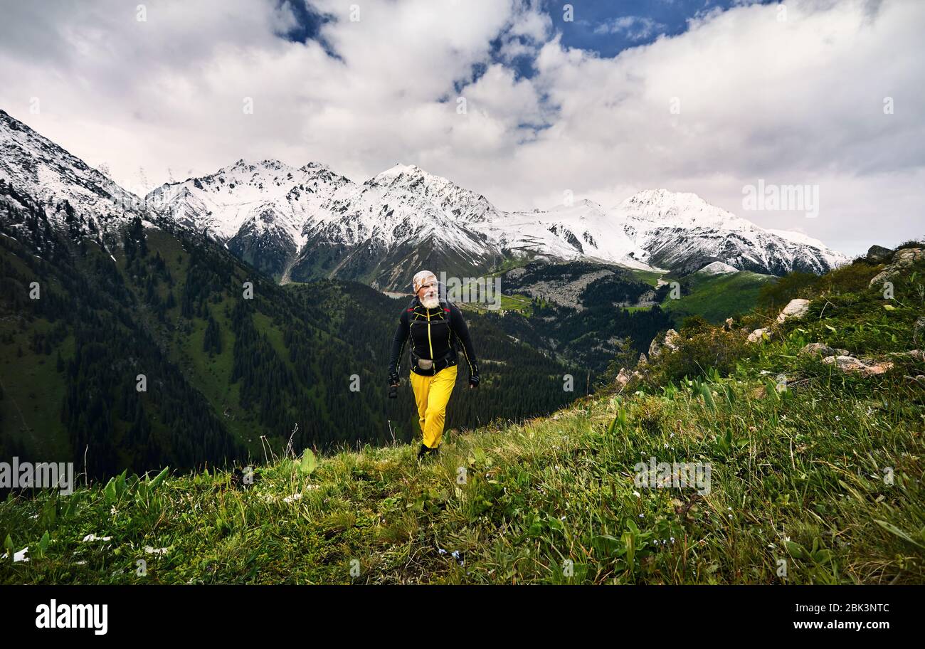 Portrait of tourist with grey beard and yellow pants in the snowy mountains. Outdoor travel concept Stock Photo