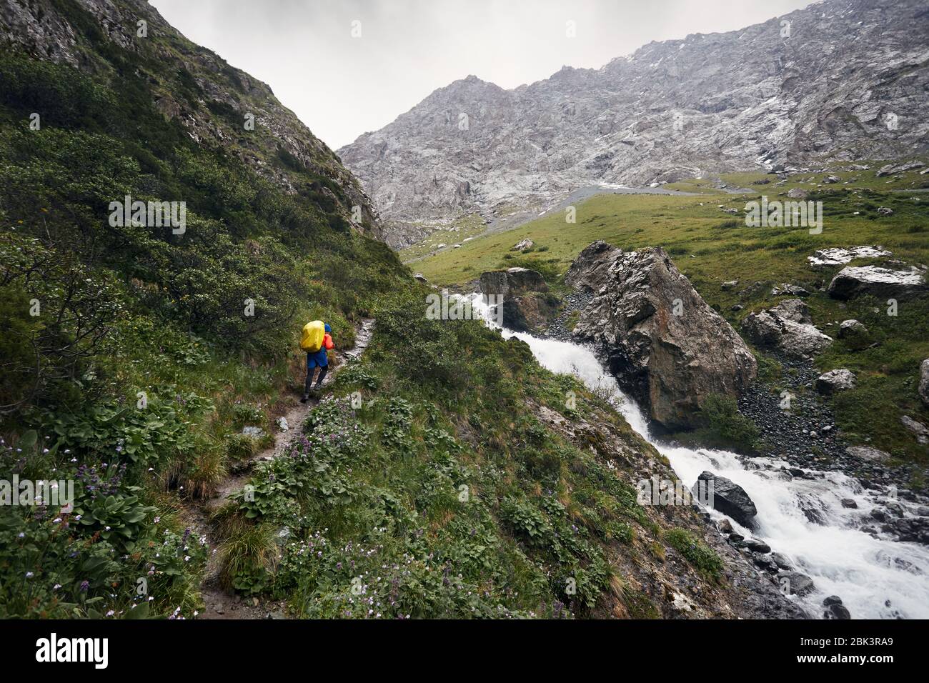 Hiker with yellow backpack in the mountain valley with river and rocky mountains in Karakol national park, Kyrgyzstan Stock Photo