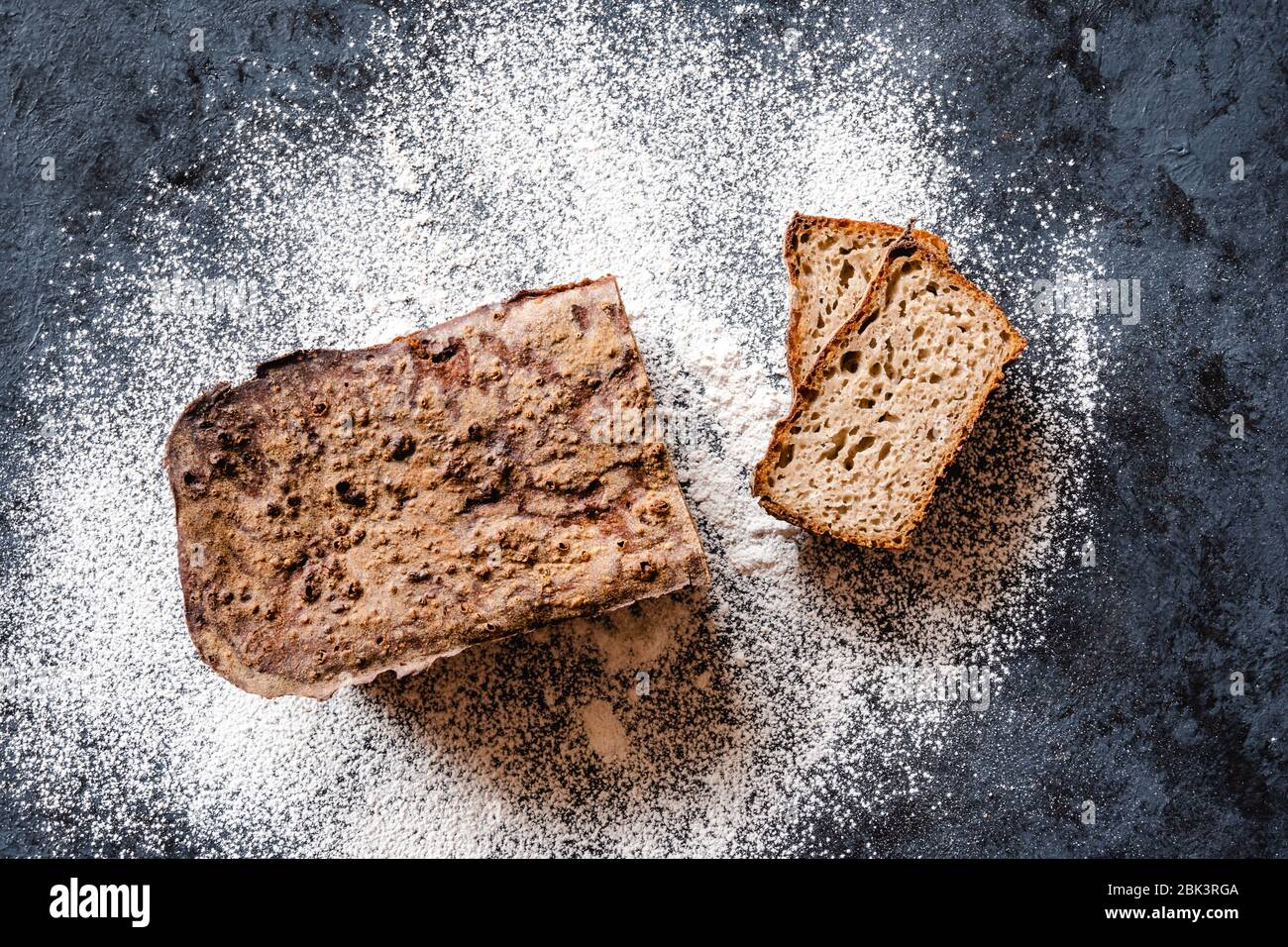 Homemade sourdough rye bread and white flour on a black background