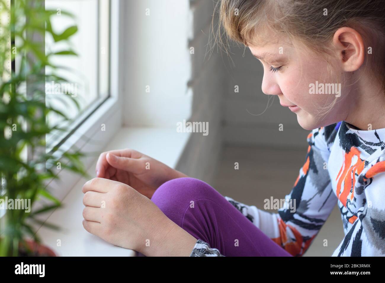 Offended girl cries at the window in the room Stock Photo