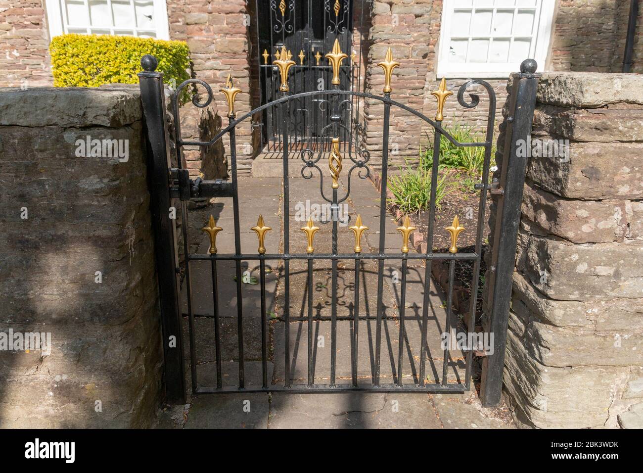 a close up view of a small black metal gate with gold spikes on attached to a stone wall Stock Photo