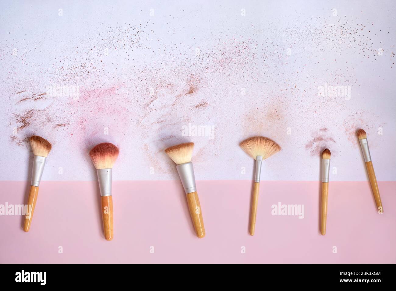 Top view of messy used eco-friendly makeup brushes with bamboo handles on white and pink background with traces of cosmetic makeup powder and blush. Stock Photo