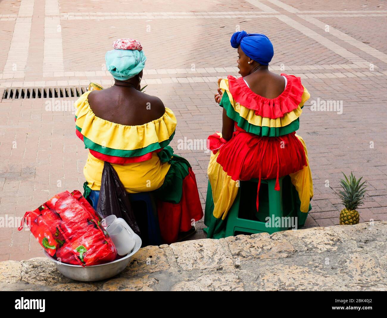 Cartagena, Colombia, August 1 2019: two tipical fruit street sellers palenqueras with colorful dresses seated resting from the back Stock Photo