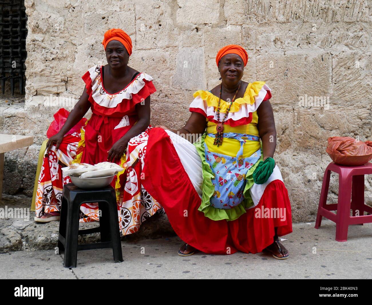 Cartagena, Colombia, August 1 2019: two tipical fruit street sellers palenqueras with colorful dresses seated resting from the front Stock Photo