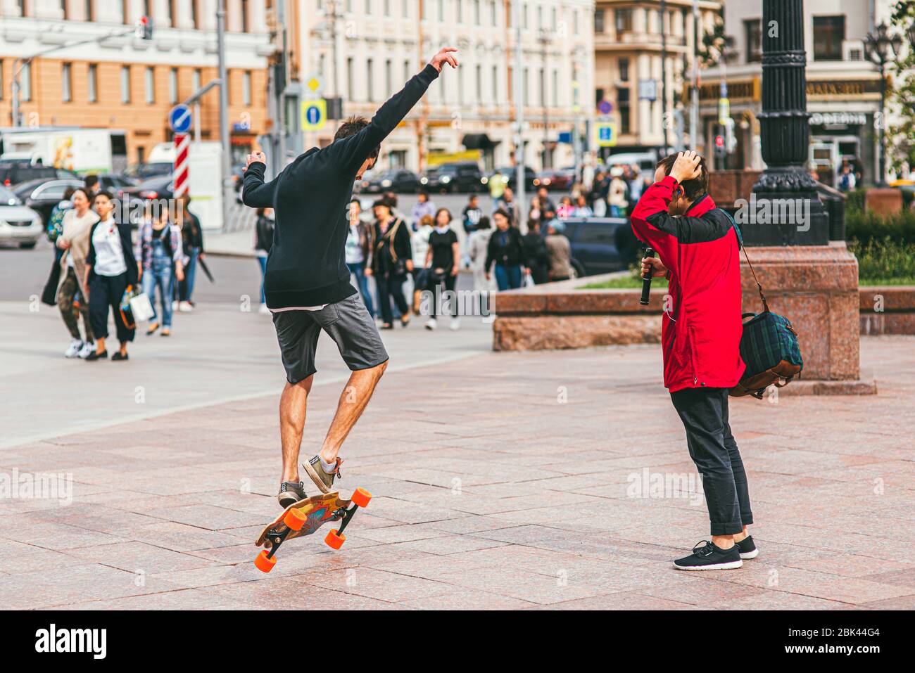 Moscow, Russia - JULY 7, 2017: young skateboarder in shorts doing a jumping trick against a crowd crossing a road Stock Photo