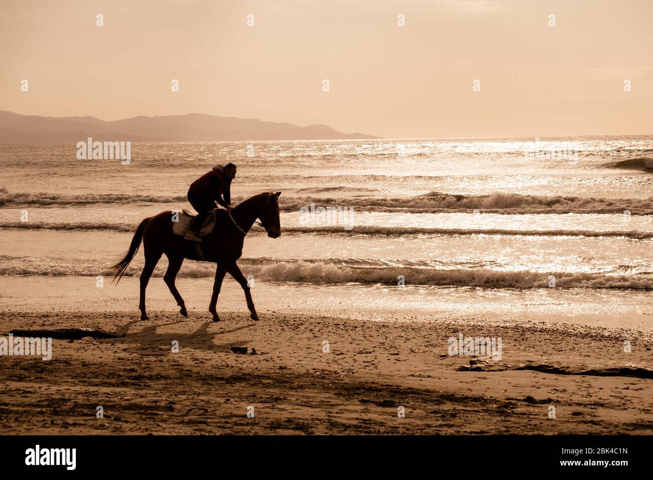 Ayia Eirini, Cyprus - 24 March, 2019: Man riding on a brown galloping horse on Ayia Erini beach in Cyprus against a rough sea Stock Photo