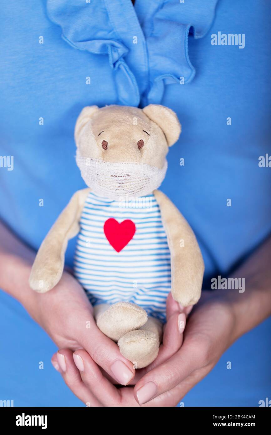 Female hands holding a cute toy teddy bear in a medical mask Stock Photo