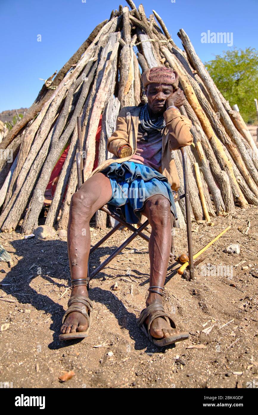 Portrait of a Himba one-handed man sitting in an old chair outside his hut. Stock Photo