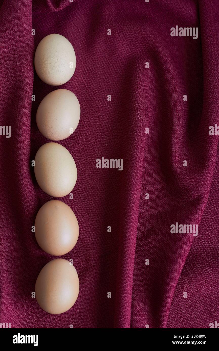 Natural eggs on red tablecloth, several brown chicken eggs lie on burgundy tablecloth, selective focus Stock Photo
