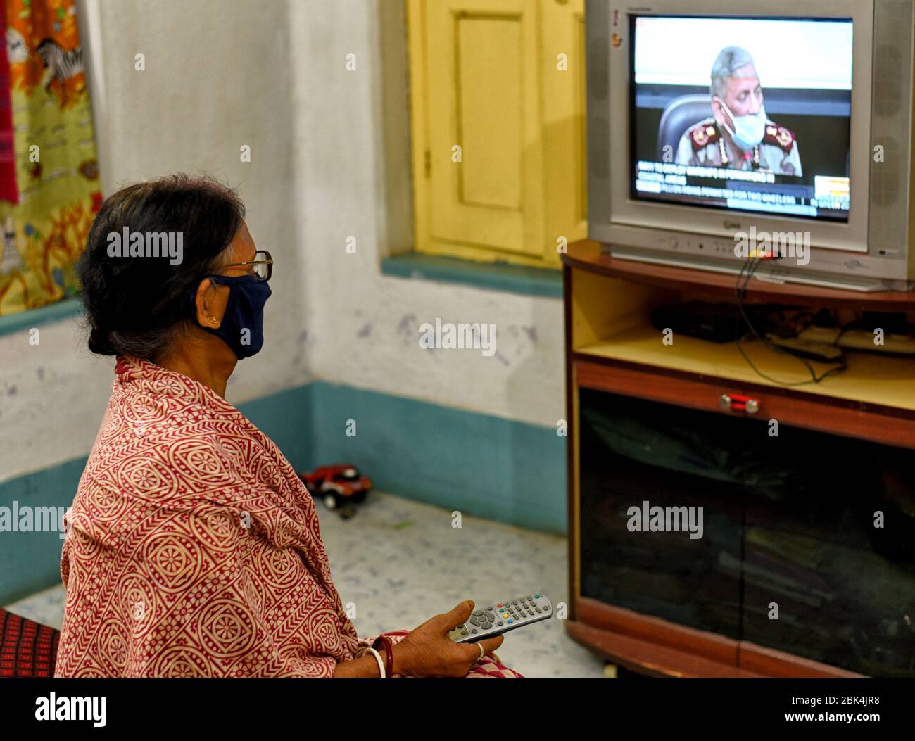 In this photo illustration a woman seen watching the Lockdown extension news on a television set while wearing a face mask as a precaution against covid-19. Stock Photo