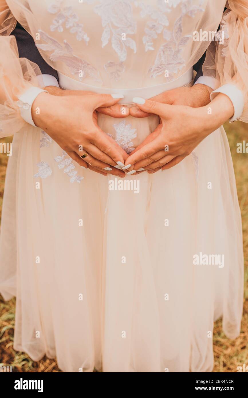 Two newlyweds holding hands on a heart shaped tummy. Wedding day. Stock Photo