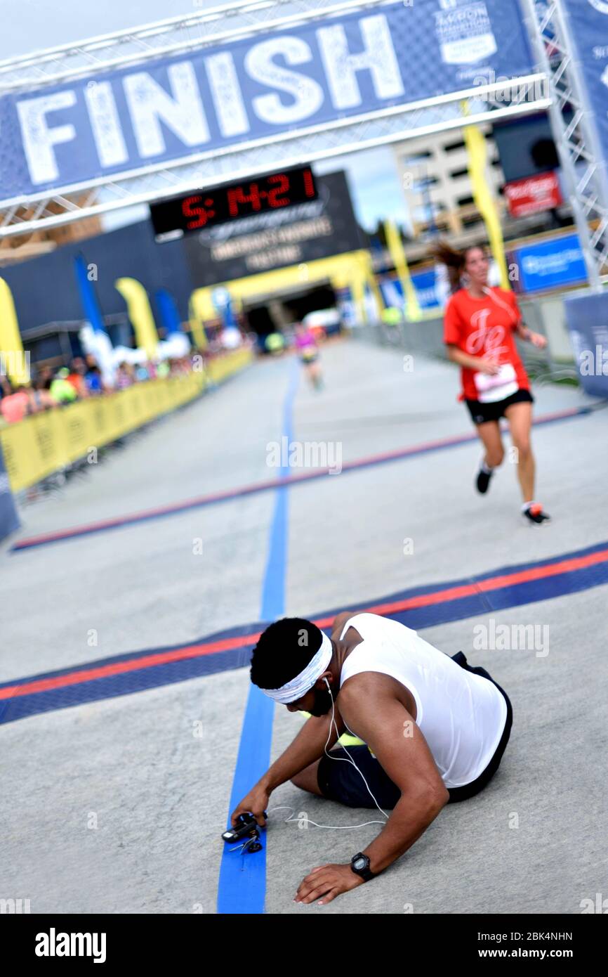 Marathon runner collapses after crossing the finish line. He's on the ground in pain and is exhausted. Stock Photo