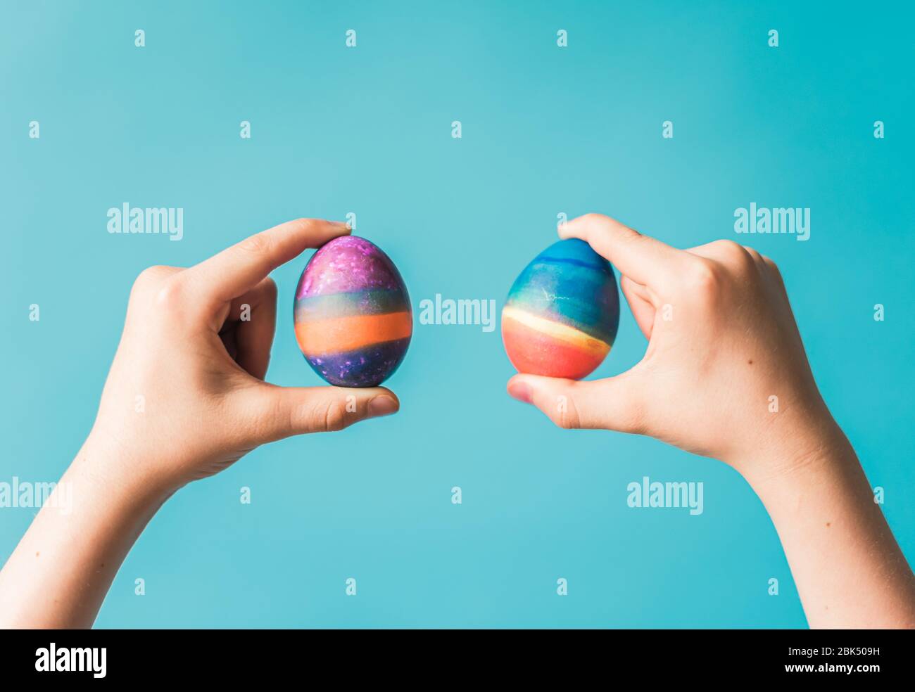 Hands holding two brightly colored easter eggs against blue backdrop. Stock Photo