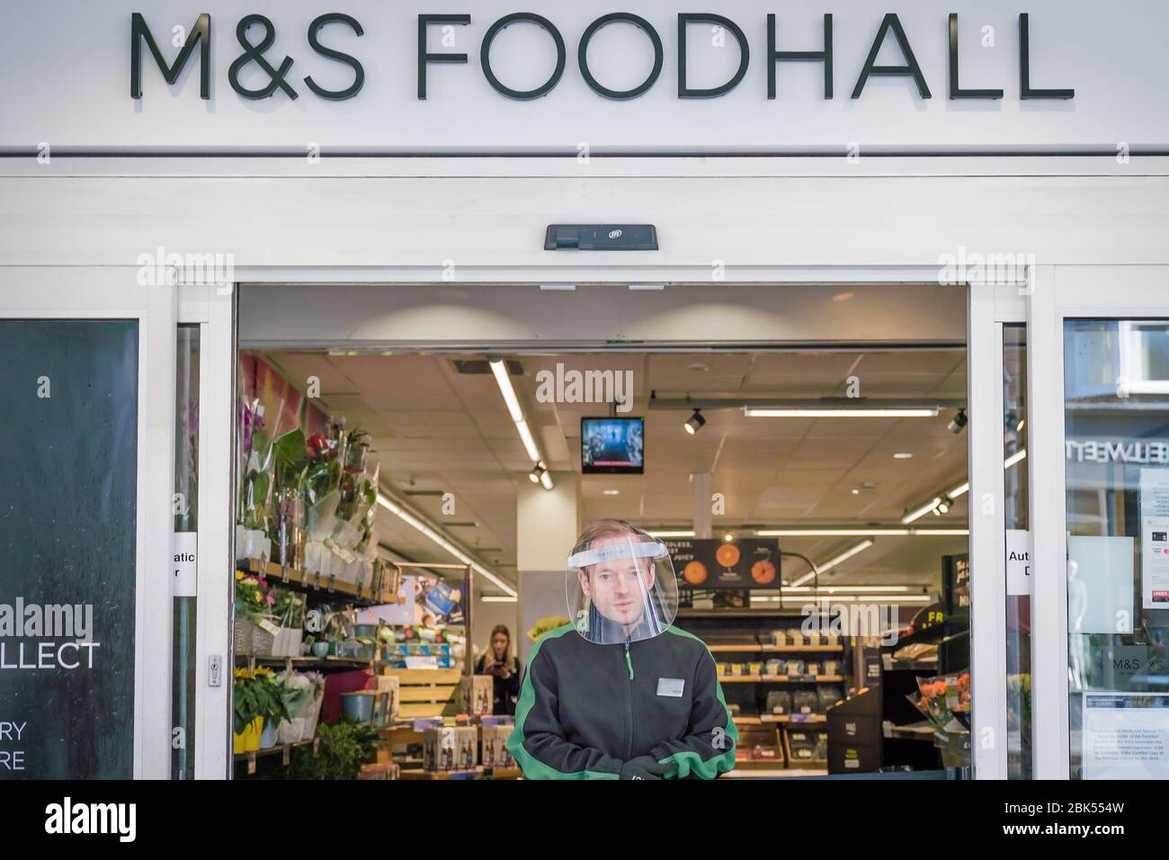 Reigate,Surrey,UK-May 1,2020 - a shop assistant wearing a face shield regulates access to M&S supermarket to prevent overcrowding and COVID-19 spread Stock Photo