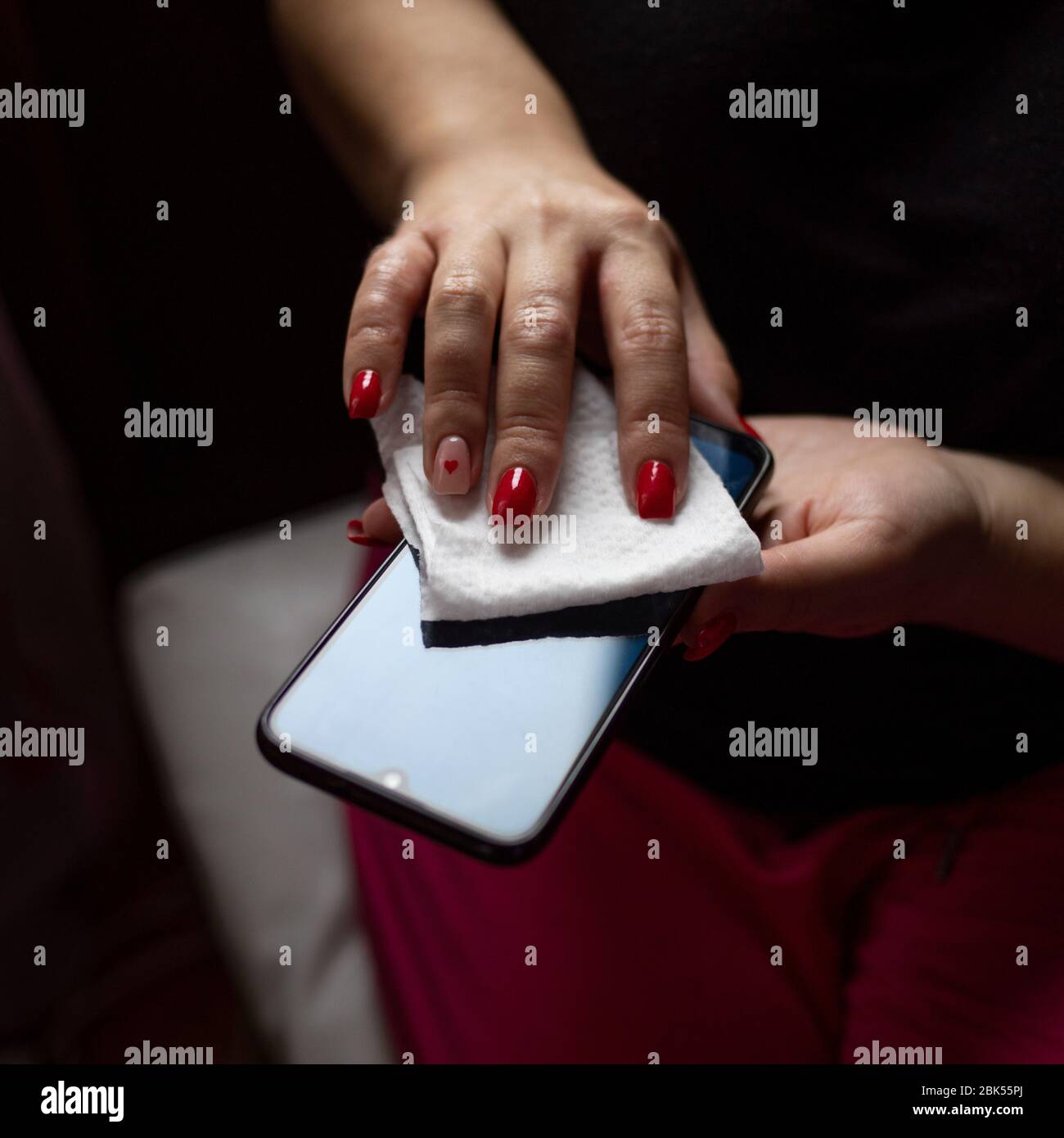 Female hands wiping mobile phone gadget with disinfectant wet wipe Stock Photo