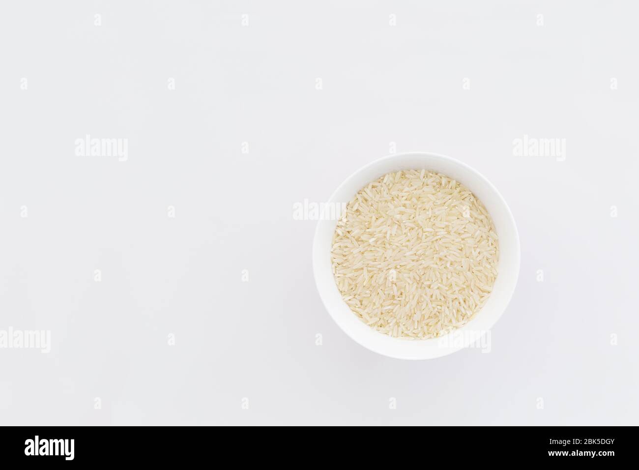 Bowl of uncooked white rice with white background. Copy space Stock Photo