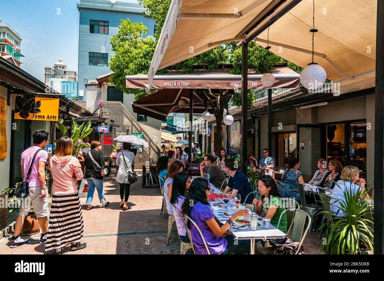People relaxing in the shade of umbrellas on a beautiful spring day at the Kommune café in Tianzifang, Shanghai, China. Stock Photo