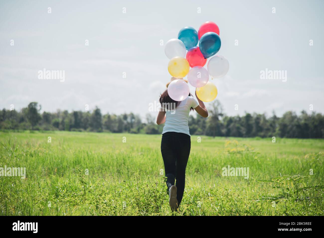 Beautiful Asian woman holding colorful balloons at meadow Stock Photo