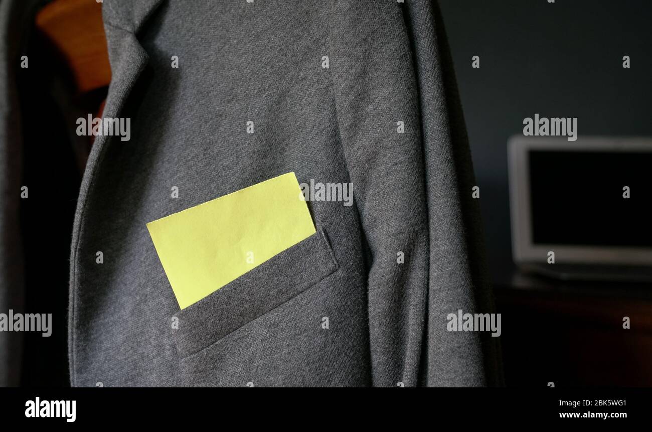 Blank yellow paper stuck out from pocket of a grey jacket. Computer laptop at the background. Space for text. Stock Photo