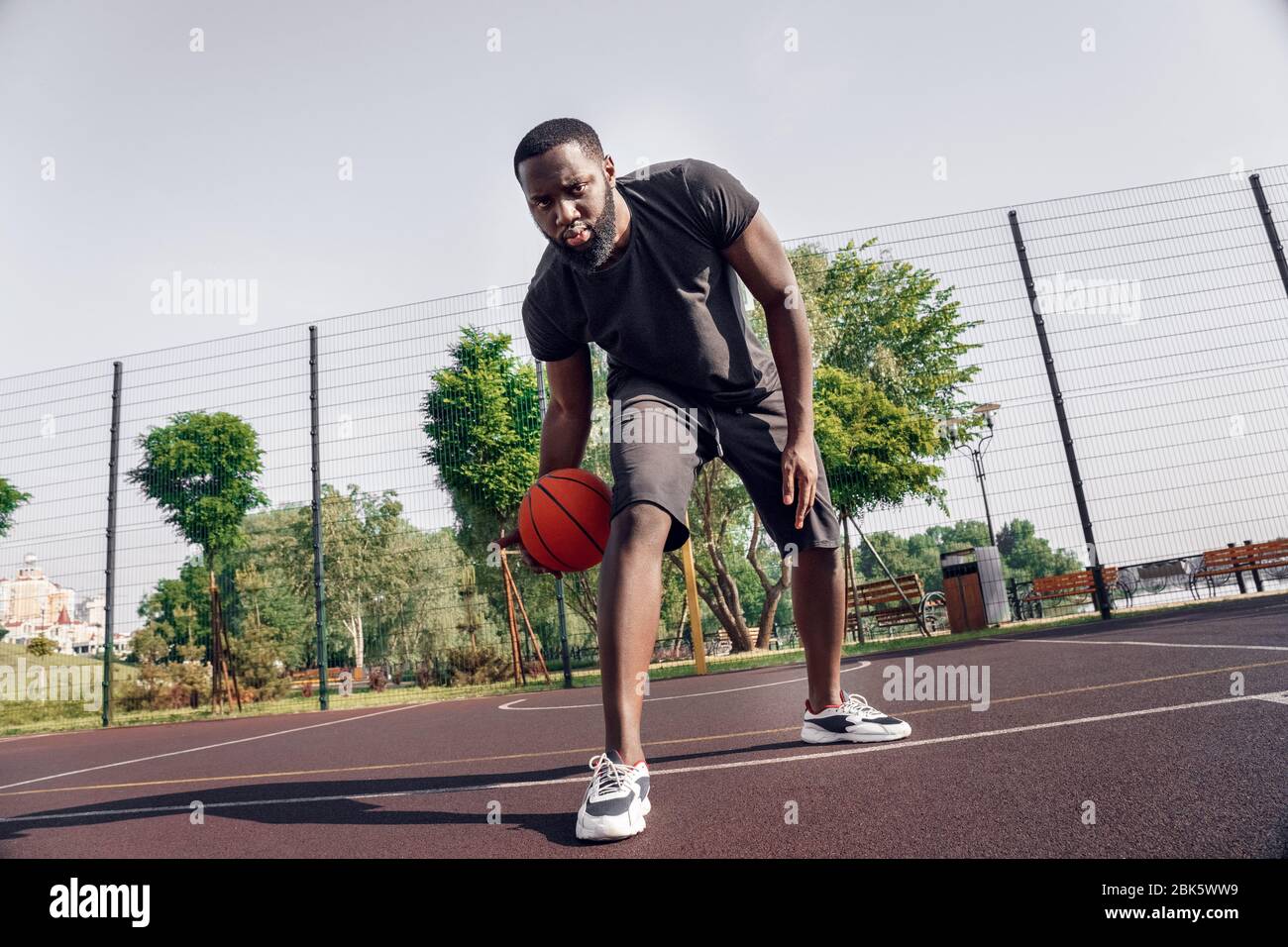 Outdoors Activity. African man playing on court dribbling ball between ...