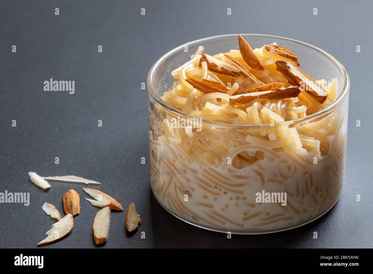 Vermicelli dessert, popular sweet dish know a kheer made with milk and garnish with dry fruits isolated on dark gray background, served in glass bowl. Stock Photo