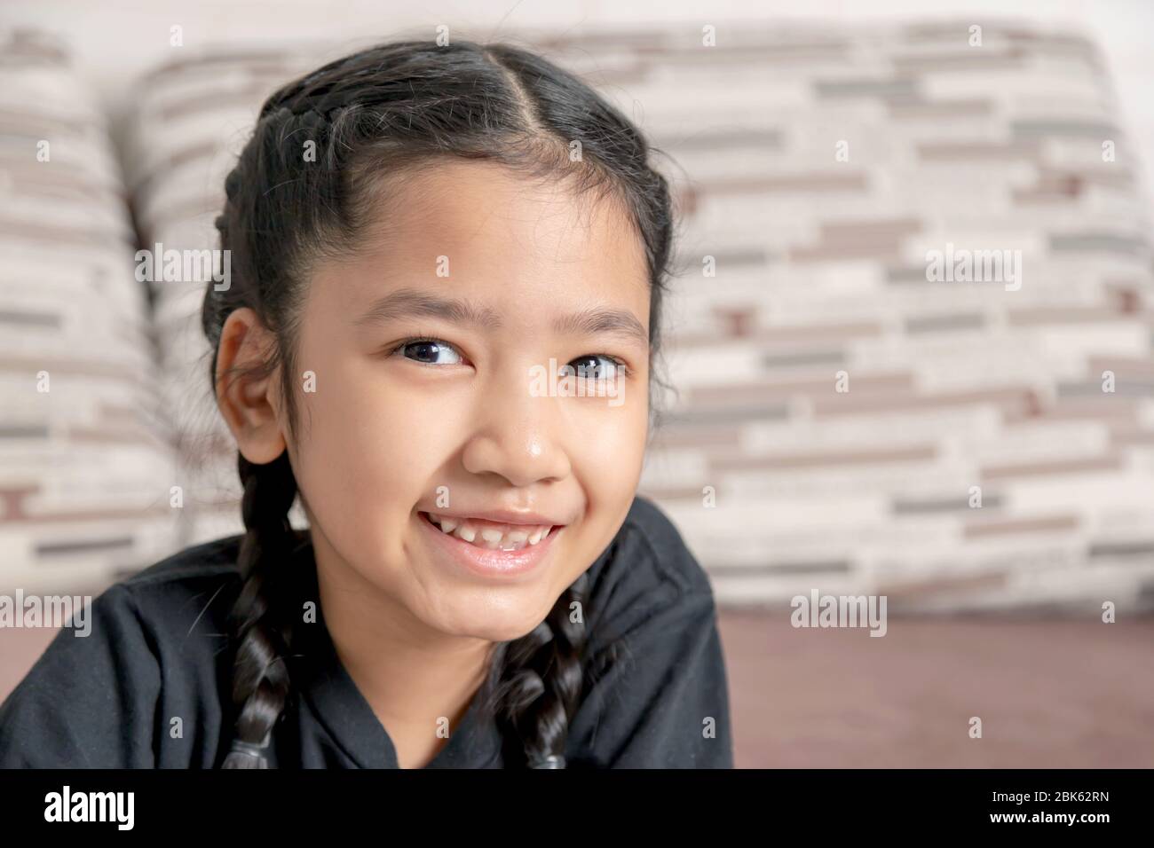 A little Asian girl in a black braid is smiling at the sofa Stock Photo